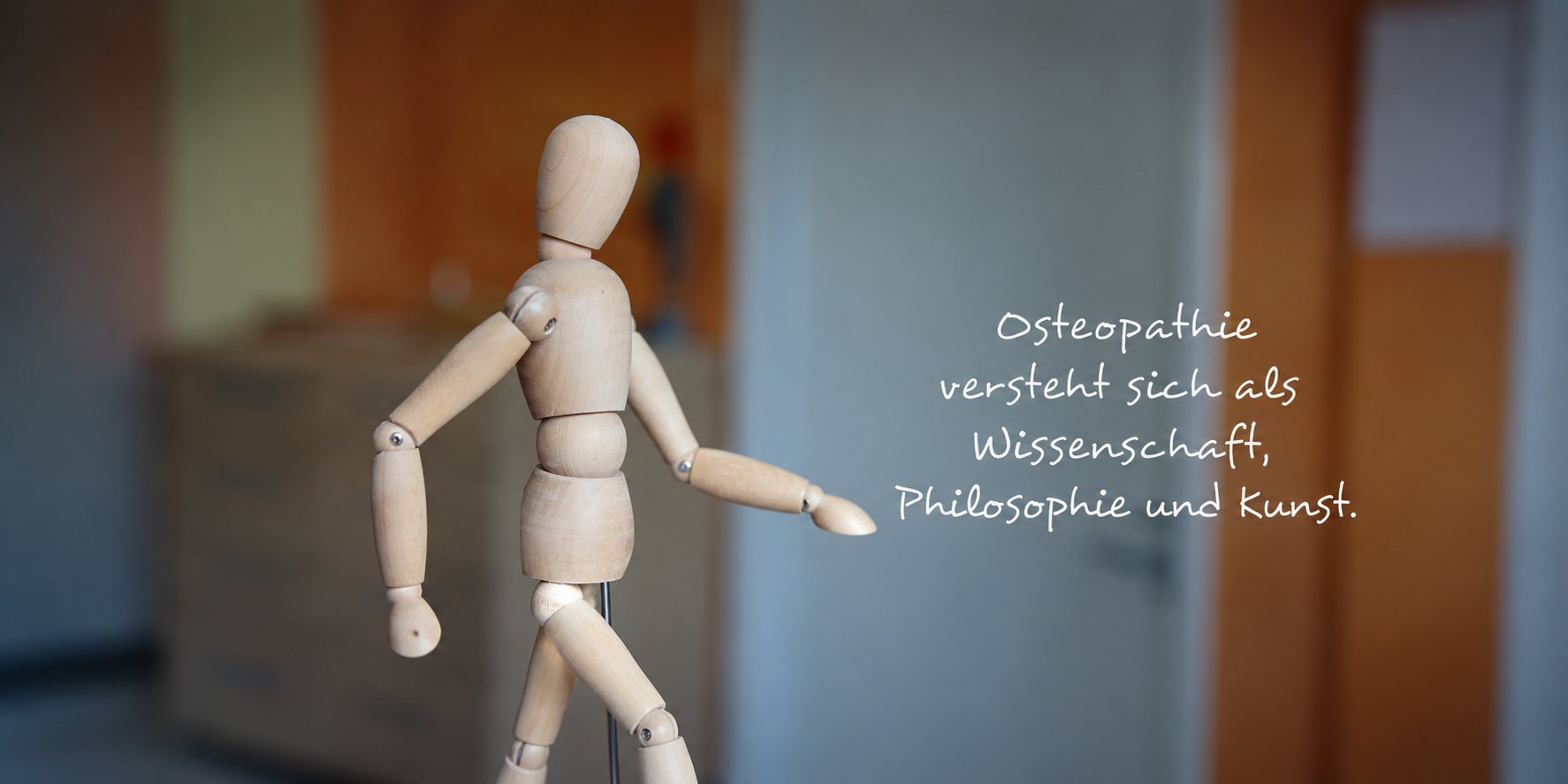 Gliederpuppe aus Holz in der Praxis Christian Klein, daneben der Satz: Osteopathie versteht sich als Wissenschaft, Philosophie und Kunst.